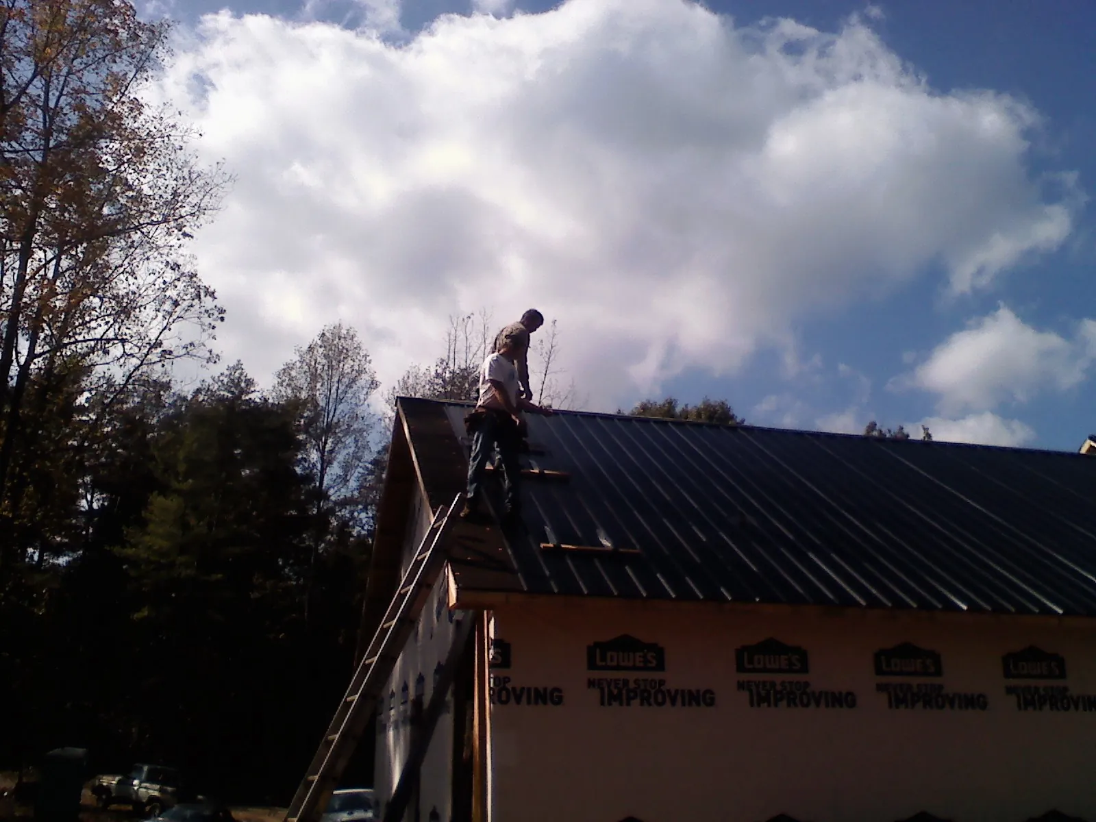Roofer fastening dark metal panels high against a cloudy sky, from a Roof Inspection job in Hartsville